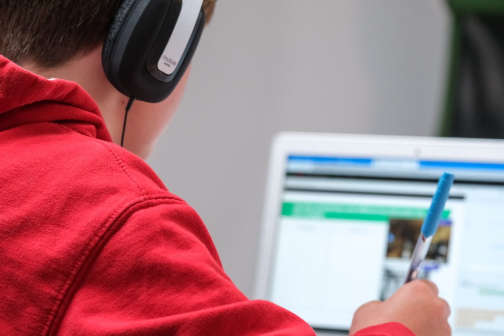 compare-fibre-Y8TiLvKnLeg-unsplash a person holding a pen and wearing headphones while looking at a laptop