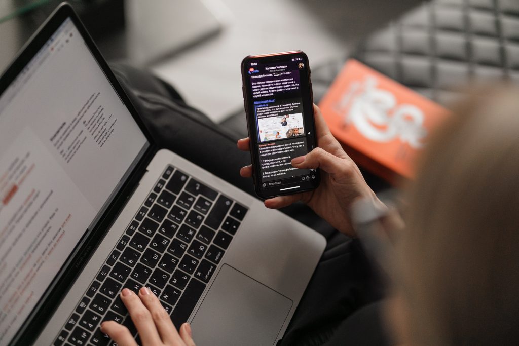 a person reading an email on a phone and typing on a laptop 